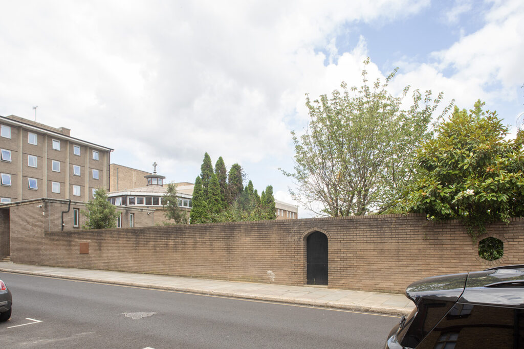 Before image: view of a low brick wall, mature trees and open sky provide a calm break along the east side of Tite Street.