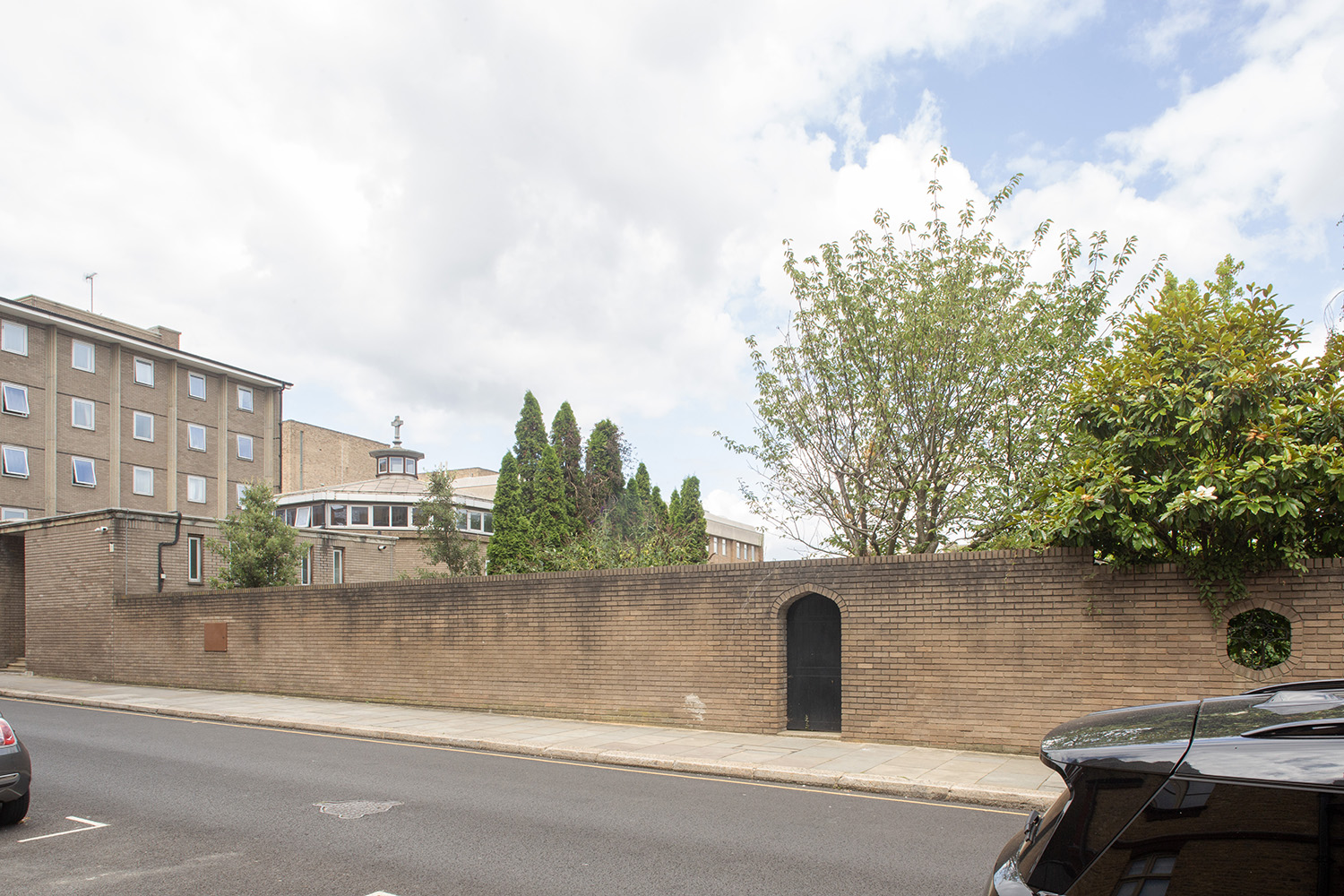 Before image: view of a low brick wall, mature trees and open sky provide a calm break along the east side of Tite Street.
